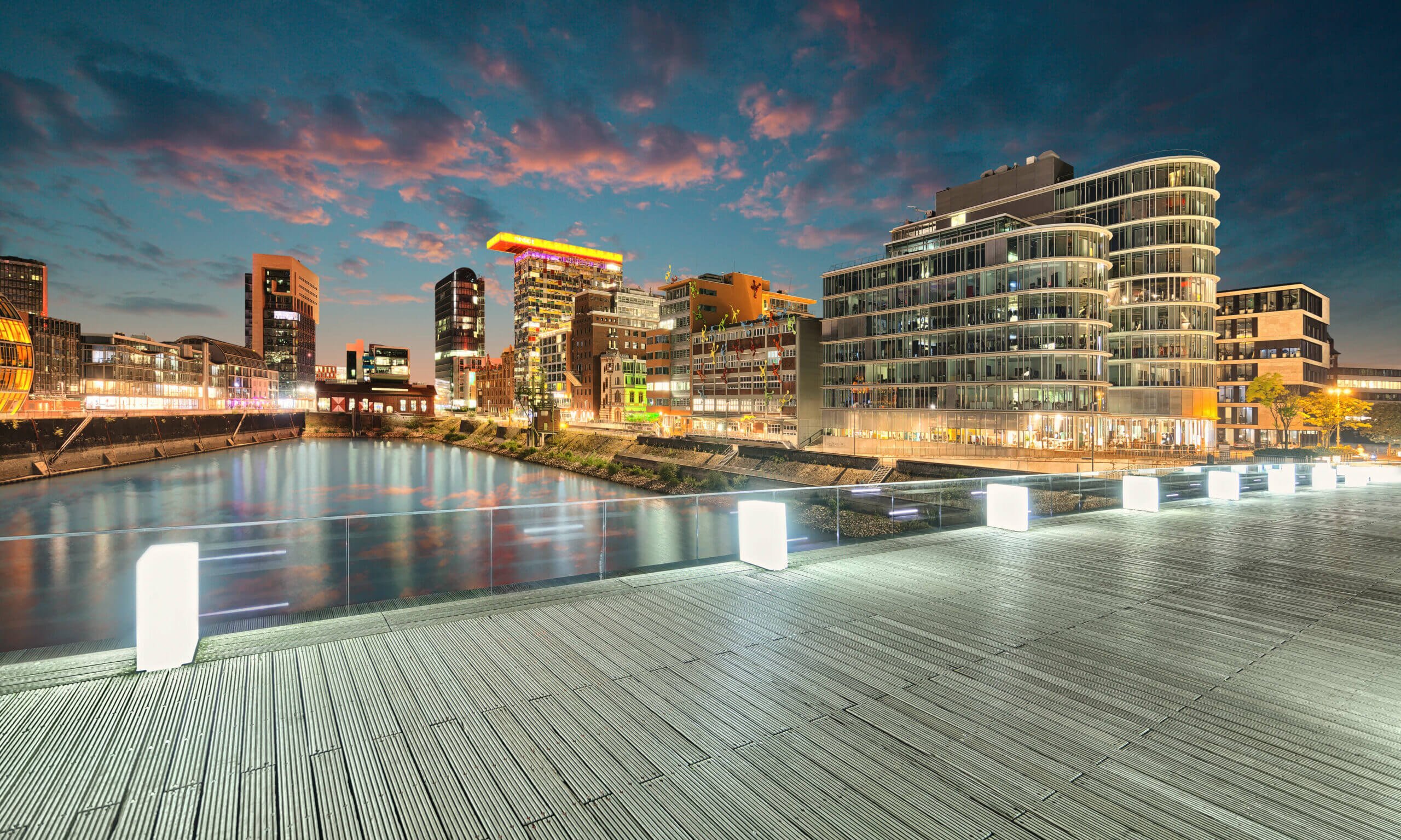 Aussicht auf leuchtende Häuserfassaden für Escort Düsseldorf von beleuchteter Holzbrücke