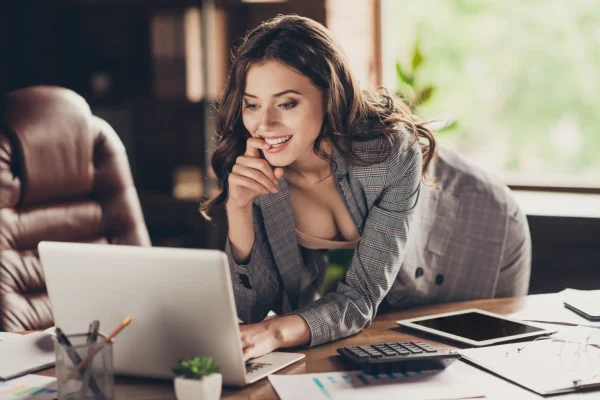 Eine anziehende Frau leicht bekleidet im Büro die stehend am Laptop arbeitet