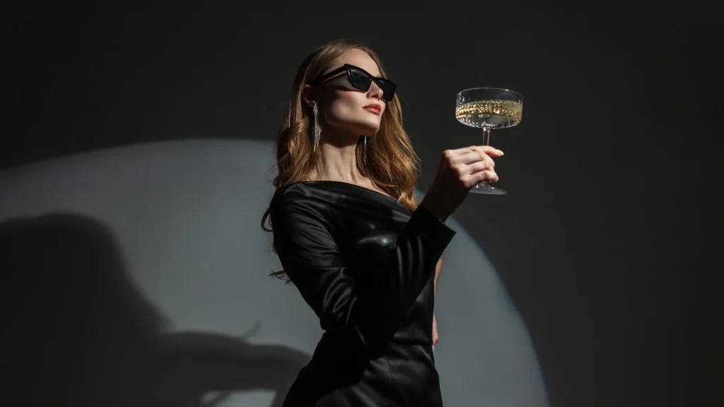 Eine Dame in einem schwarzen Abendkleid hält ein Glas Sekt in der Hand, bereit zum Anstoßen.